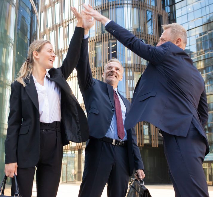 Three cheerful businesspeople giving five and smiling. Confident happy colleagues celebrating successful deal together, standing outdoors and rising hand up. Teamwork and partnership concept